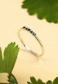 Guldring med en rad av fem små, runda blå ädelstenar som är inlagda längs toppen. Slät, polerad yta med en smal design.