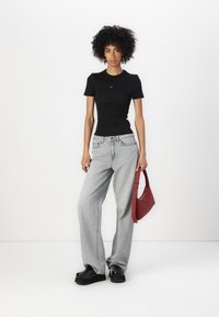 T-shirt nera attillata a maniche corte, jeans larghi grigio chiaro, scarpe con plateau nere e borsa a spalla rossa. Design semplice, senza fantasie.