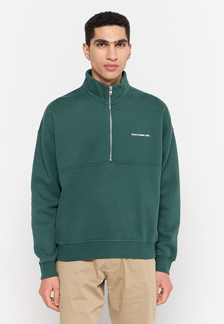 Groen fleece pullover met hoge kraag, voorzien van een korte rits en een logo op de linker borst. Zachte textuur en een ontspannen pasvorm.