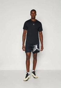 Čierne tričko s malým bielym logom, čierne šortky s bielym abstraktným vzorom a krémové topánky s čiernymi akcentmi.