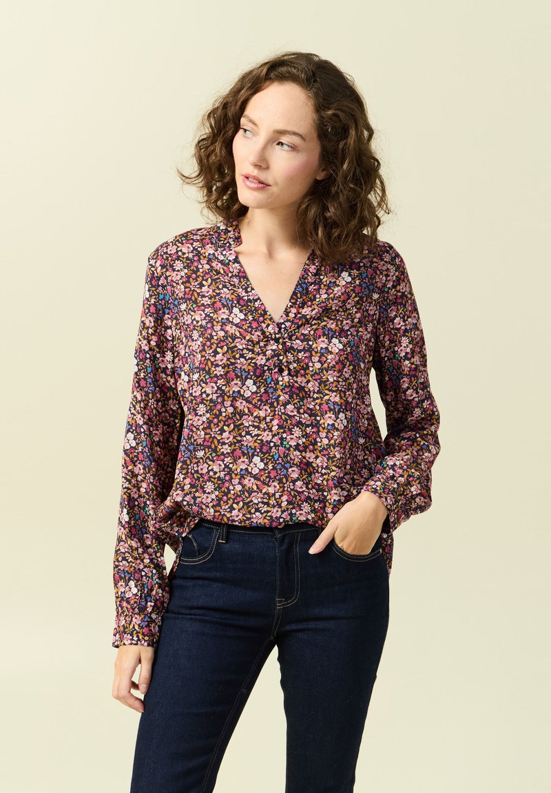 Långärmad blommig blus med djup v-ringning, med en mörk bakgrund och flerfärgade blommönster. Bärs med mörka jeans.