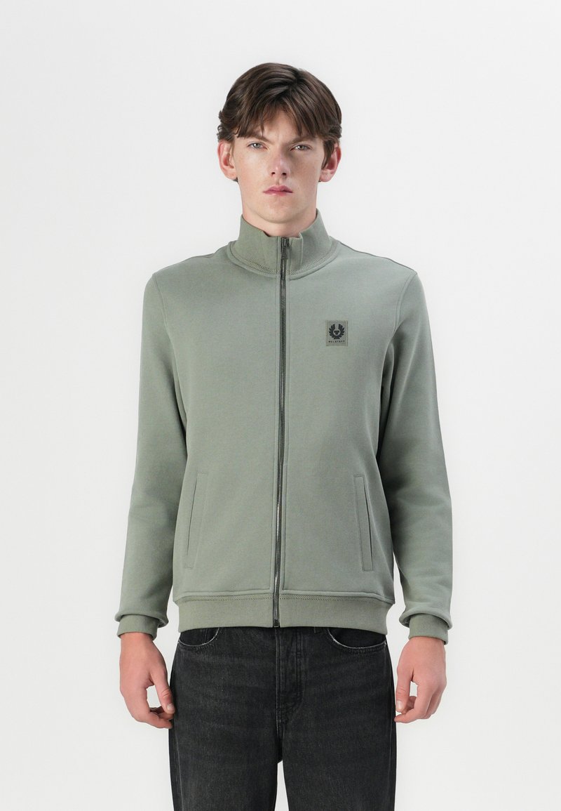 Light green zip-up jacket with a high collar, side pockets, and a logo patch on the chest. Made from a soft, smooth fabric.