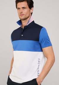 Polo-shirt met korte mouwen in marineblauw, blauw en wit met kleurvlakken. Voorzien van een geknoopte kraag met gestreepte binnenvoering en gedrukt tekst aan de zijkant.