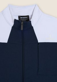 Chaqueta con cremallera en azul marino y blanco, con cuello alto, tejido texturizado, bolsillo delantero y logo bordado en el pecho.