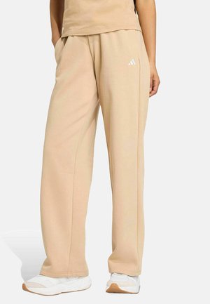 Pantaloni jogger beige realizzati in tessuto morbido, dotati di tasche laterali e logo Adidas bianco. Vestibilità ampia con gambe dritti e una vita comoda.