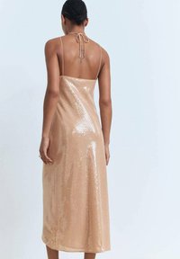 Vestido de lentejuelas nude con corte recto, tirantes finos y lazo en la parte posterior. Su textura brillante y longitud hasta la mitad de la pantorrilla realzan su elegancia.