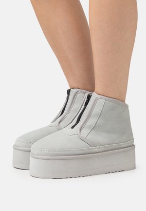 Šedé semišové kotníkové boty s platformovou podrážkou a dvěma předními zipy. Hladký povrch s jednoduchým designem a bez viditelných vzorů nebo akcentů.