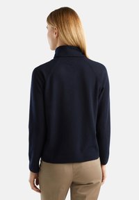 Granatowy sweter z wysokim kołnierzem, prążkowanymi mankietami i dołem, o gładkiej fakturze i kroju raglanowym.