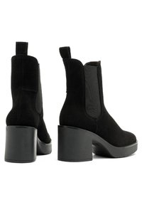 Botines de ante negro con paneles elásticos en los laterales, tacones gruesos y tiradores para facilitar su uso. Suela texturizada para un mejor agarre y estabilidad.