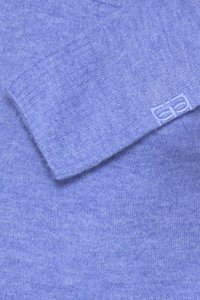 Manche de pull en tricot bleu clair doux avec bord-côtes et petit logo brodé près du poignet.