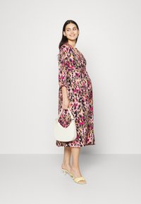 Vestido midi de estampa de leopardo cor-de-rosa com mangas três quartos e uma cintura amarrada, combinado com uma bolsa branca e sandálias de salto amarelas.