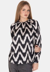Blusa a righe zigzag in bianco e nero con maniche lunghe, scollo rotondo e tessuto liscio. Nota per i suoi colori contrastanti e la sua texture.