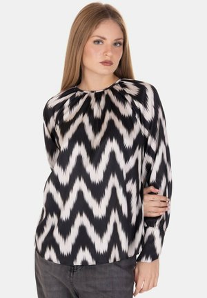 Blusa a righe zigzag in bianco e nero con maniche lunghe, scollo rotondo e tessuto liscio. Nota per i suoi colori contrastanti e la sua texture.