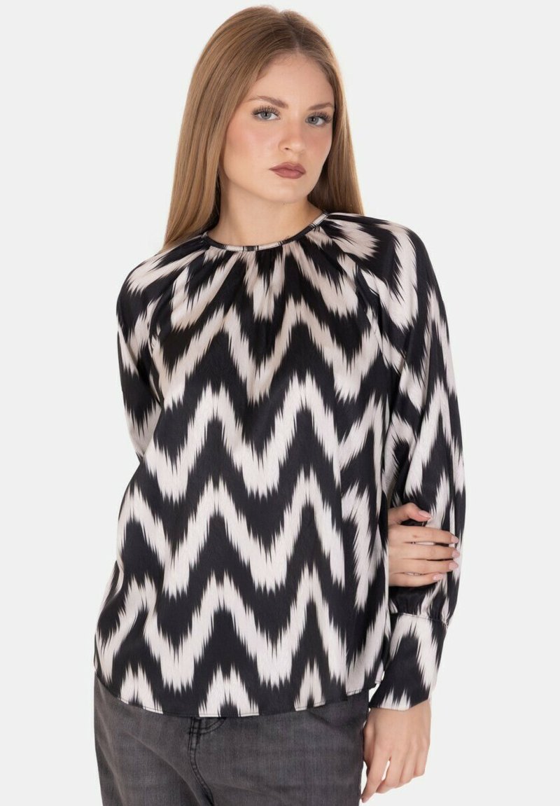Blusa a righe zigzag in bianco e nero con maniche lunghe, scollo rotondo e tessuto liscio. Nota per i suoi colori contrastanti e la sua texture.