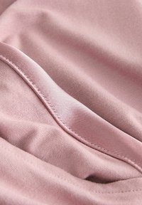 Tessuto rosa chiaro con una superficie liscia e una leggera lucentezza. Presenta bordi cuciti con cura e morbide pieghe, che mettono in risalto il gioco di luci.