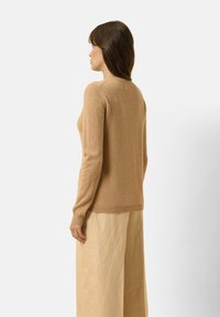 Lichtbruine wollen trui met een ronde halslijn, lange mouwen en een zachte textuur, gecombineerd met crèmekleurige wijde broek.