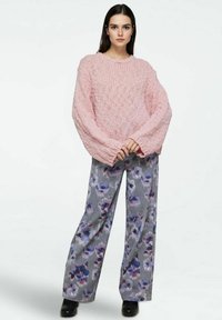 Maglione rosa oversize lavorato a maglia con maniche larghe, abbinato a pantaloni grigi a gamba larga con un motivo floreale viola e stivaletti neri alla caviglia.