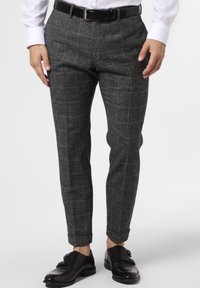 Grå rutiga byxor med smal passform, tillverkade i texturerat tyg. Har en slät framdel och uppvikta byxben, i kombination med svarta dresskor.