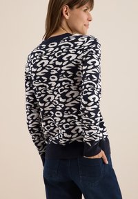Pull marin avec imprimé léopard blanc, col rond, ourlet et poignets côtelés. Texture en tricot douce, manches longues et coupe décontractée.