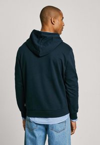 Sudadera azul marino con capucha ajustable, hecha de una suave mezcla de algodón. Presenta un corte holgado y puños acanalados en las mangas.