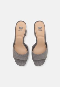 Escarpins gris en tissu à enfiler avec une large sangle supérieure et un dos ouvert. Semelle intérieure lisse beige avec logo. Talon bloc bas. Extérieur texturé.