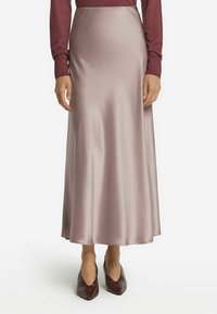 Satin-maxikleid in hellem Mauve mit glatter Textur. Verfügt über eine ausgestellte Silhouette und eine hohe Taille, kombiniert mit spitzen kastanienbraunen Schuhen.
