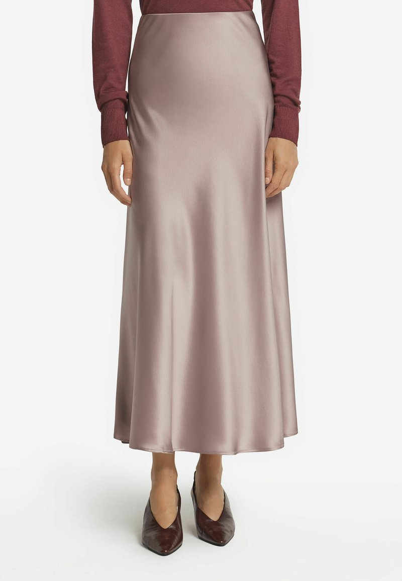 Satin-maxikleid in hellem Mauve mit glatter Textur. Verfügt über eine ausgestellte Silhouette und eine hohe Taille, kombiniert mit spitzen kastanienbraunen Schuhen.