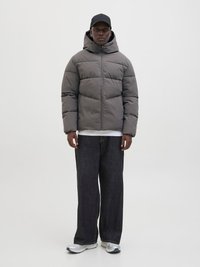 Grå vadderad jacka med huva, med dragkedja och quiltat mönster. Kombinerad med mörka vida jeans och gråa träningsskor.