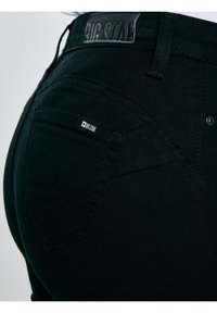 Zbliżenie na tylnią kieszeń czarnych dżinsów z dżinsu, z przeszyciami i metką marki "Big Star" na kieszeni oraz pasie.