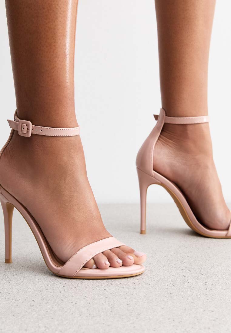 Las sandalias de tacón alto rosa presentan una correa en el tobillo con hebilla, un diseño de punta abierta, una textura de cuero suave y tacones delgados y de aguja.