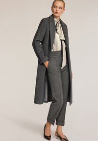 Grijze wollen jas met een slanke pasvorm, gecombineerd met een crèmekleurige blouse en op maat gemaakte grijze geruiten broek. Bevat een strik en glanzende schoenen.