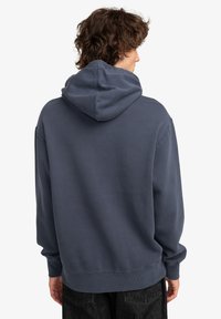 Sudadera azul marino con una textura suave, bolsillo canguro y capucha ajustable con cordón. Corte ligeramente holgado, puños y dobladillo acanalados.