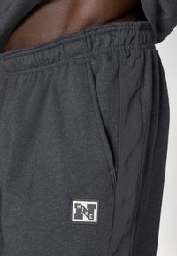 Tamno sivi dukserice hlače od mekog materijala, s elastičnim strukom, bočnim džepovima i malim Nike logom na vanjskoj strani bedra.