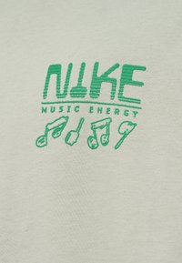 Svetlo zelena bombažna majica s zelenim vezenim napisom "NIKE MUSIC ENERGY" in ikonami glasbenih not spodaj.