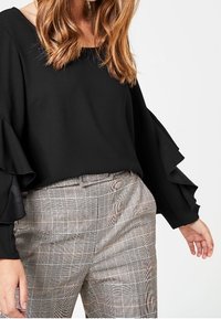 Black blouse with ruffled sleeves paired with light check-pattern trousers, featuring a tailored fit and a smooth texture.