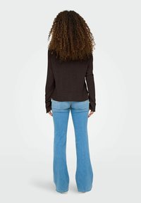 Blusa oscura de manga larga combinada con unos vaqueros de campana de color azul claro. La blusa es holgada con mangas largas, y los vaqueros tienen un acabado ligeramente deslavado.
