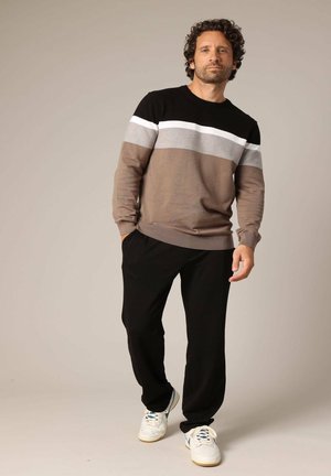Pull en color-block pour homme en marron, beige, gris et noir avec un col rond ; associé à un pantalon noir et des baskets blanches.