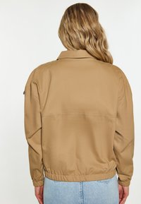 Khaki bomber jacket o luźnym kroju, z elastycznym pasem i długimi rękawami. Gładka faktura, mała kieszeń po bokach.