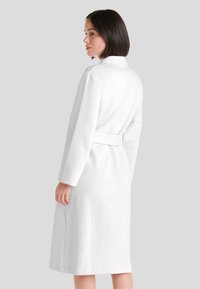 Bata de baño blanca, de longitud hasta la rodilla, con un patrón texturizado, mangas largas y un cinturón atado en la cintura. Tela suave con un diseño rico.