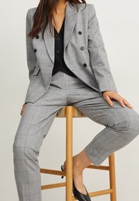 Blazer de lana a cuadros grises de doble botonadura combinado con pantalones a medida a juego. Top negro debajo y zapatos negros sin cordones. Textura de tela suave.