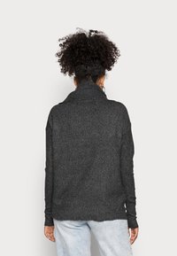 Mörkgrå stickad tröja med hög krage, sänkta axlar och ribbade muddar. Har en avslappnad passform och en fransig nederdel.