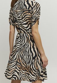 Lyhythihainen mekko musta-beige zebrakuosilla. Ominaisuuksiin kuuluu kootusti vyötäröltä ja levenevä hameosa, joka tarjoaa mukavan istuvuuden. Sileä pinta.