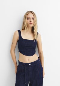 Tamni plavi traperi crop top s kvadratnim izrezom i širokim trakama, s vertikalnim šavovima i lagano zakrivljenim rubom.