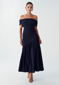 Robe bleu marine à épaules dénudées avec tissu texturé, corsage ajusté et jupe évasée ; présente des coutures diagonales et un ourlet fluide.