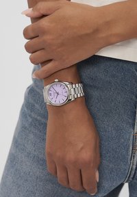 Orologio argentato con cassa rotonda e quadrante lilla. Numeri romani a 12, 3, 6 e 9, e bracciale in acciaio inossidabile a maglie. Design semplice.