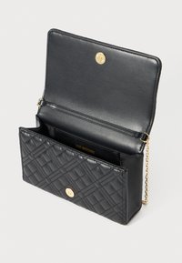 Zwarte gekwilt leren handtas met gouden drukknoopsluiting, een open flap en een dunne gouden schouderband tegen een witte achtergrond.