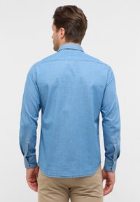 Lichtblauwe denim overhemd met lange mouwen, knoopmanchetten en een afgeronde zoom. De stof lijkt glad met een lichte glans.