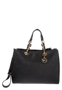 Sac à main en cuir noir avec des poignées en chaîne dorée et un pendentif circulaire au logo MK, comprenant une bandoulière détachable.