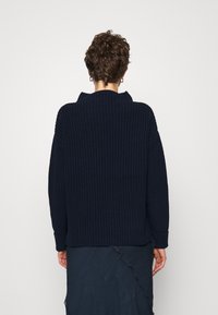 Granatowy dzianinowy sweter z kołnierzem złożonym, opuszczonymi ramionami i prążkowanymi mankietami. Charakteryzuje się fakturowanym wzorem i luźnym krojem.