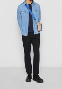 Camicia di denim azzurro, t-shirt navy, pantaloni neri e stivaletti neri con lacci. Borsa a tracolla beige con dettagli blu.